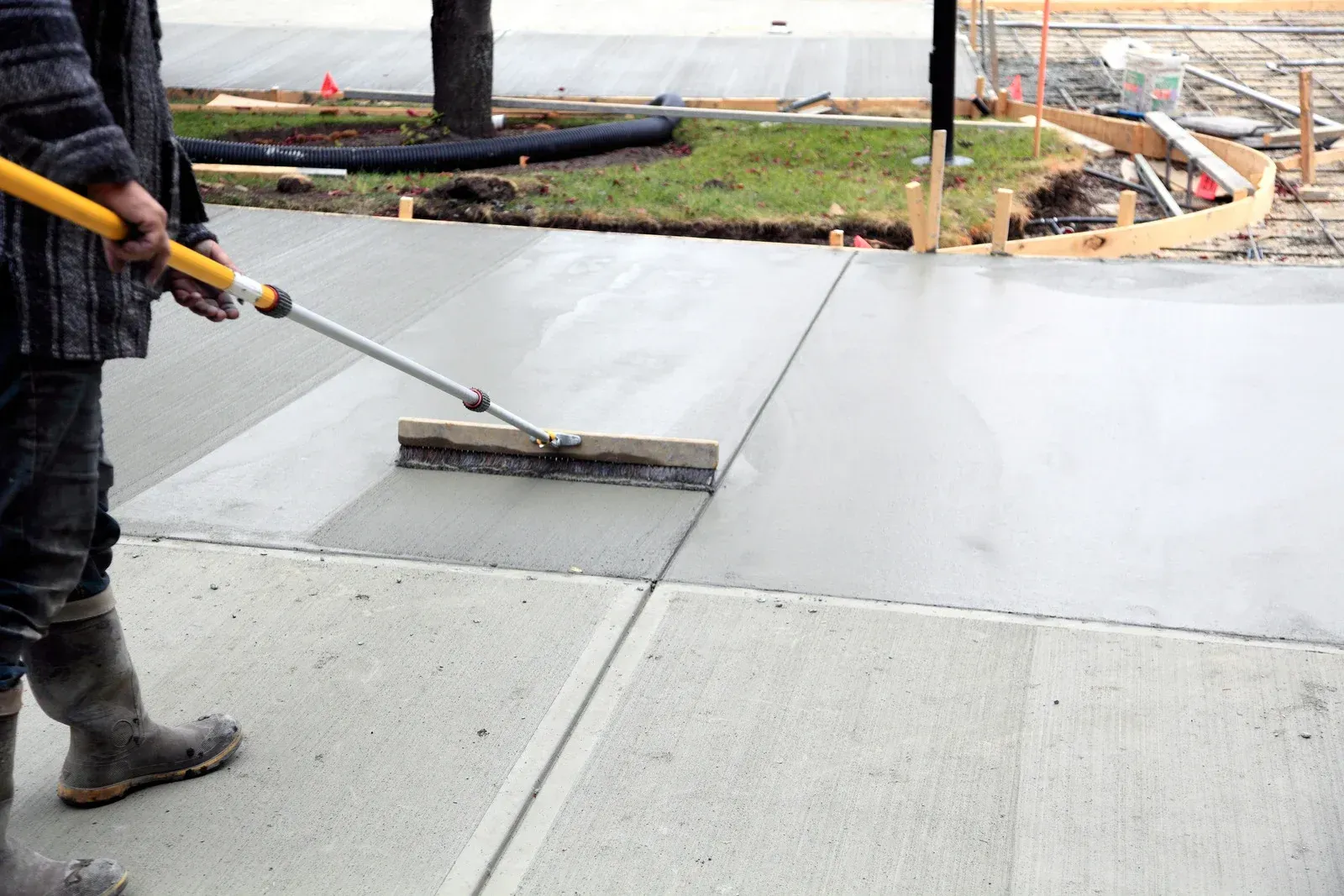 Worker smoothing wet concrete with a long-handled trowel on a driveway construction site