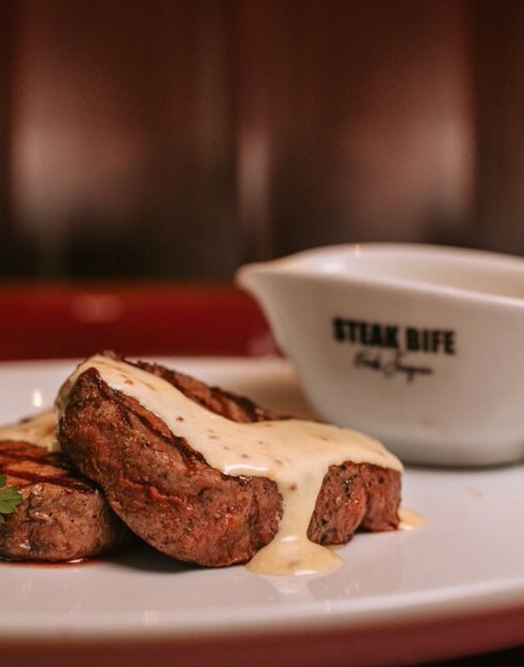 Bife coberto com molho cremoso em um prato branco ao lado de uma molheira.