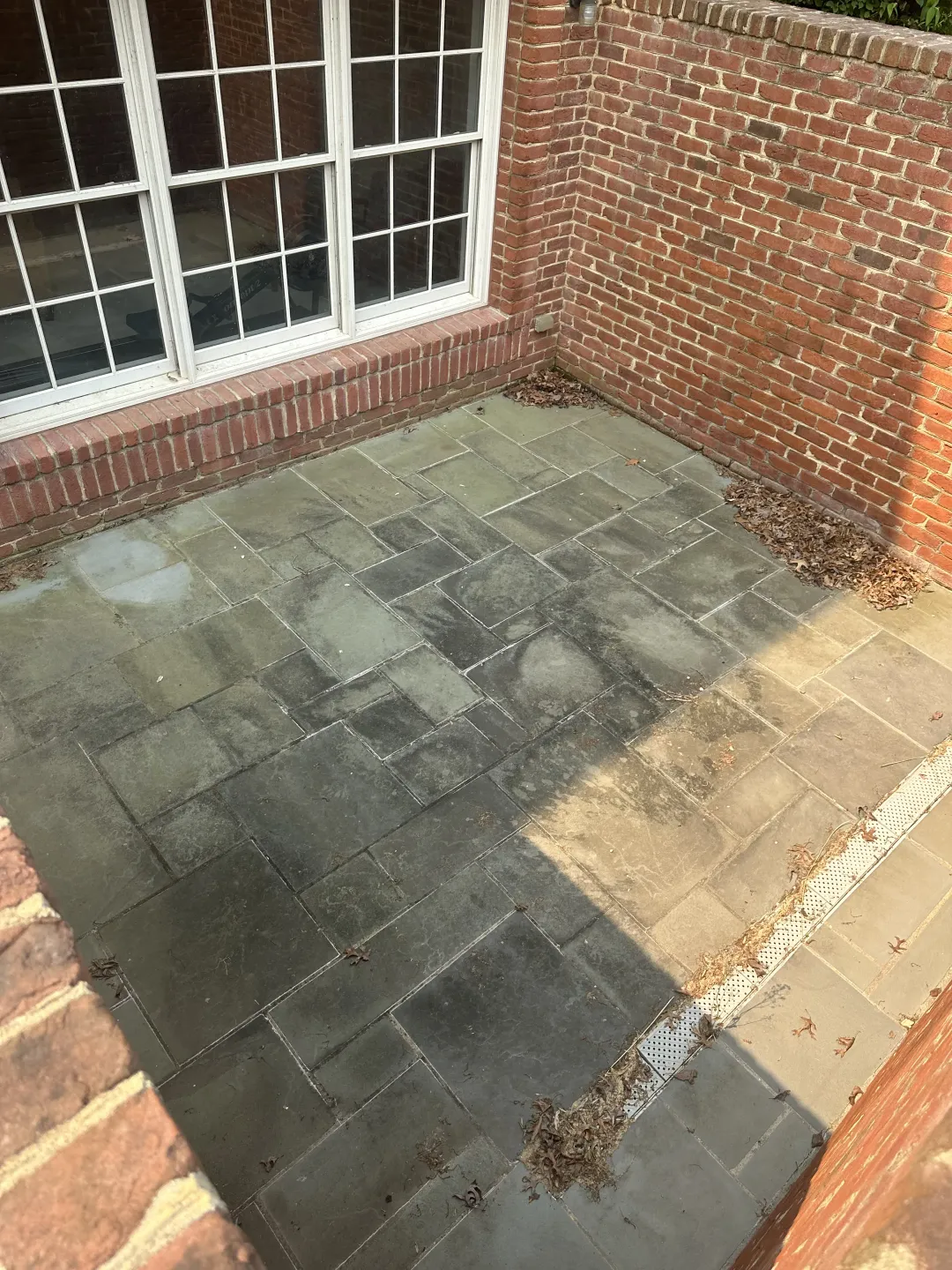 Brick patio with dark and light paving stones beside a windowed brick wall.