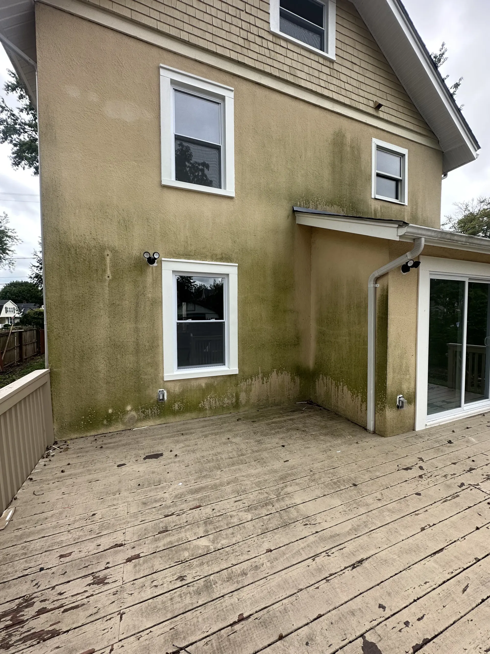 Moss-stained beige house exterior with a wooden deck and sliding glass door