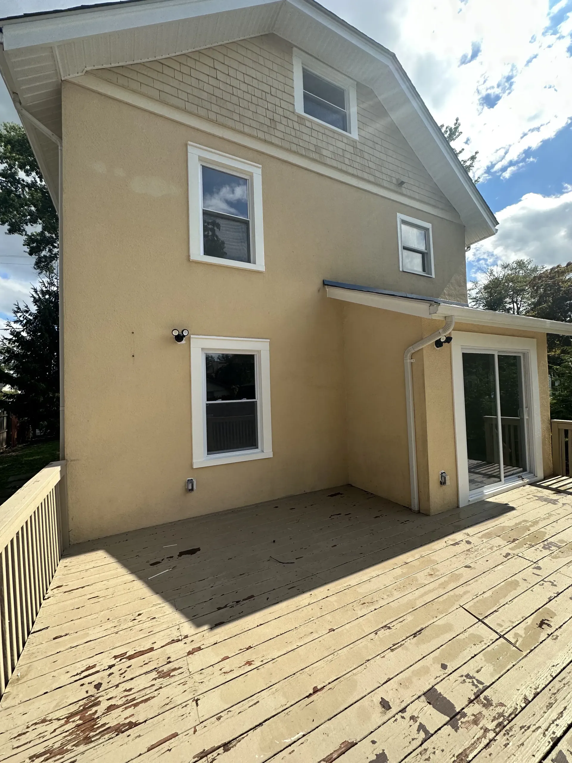 Beige house exterior with a wooden deck and sliding glass door under a partly cloudy sky
