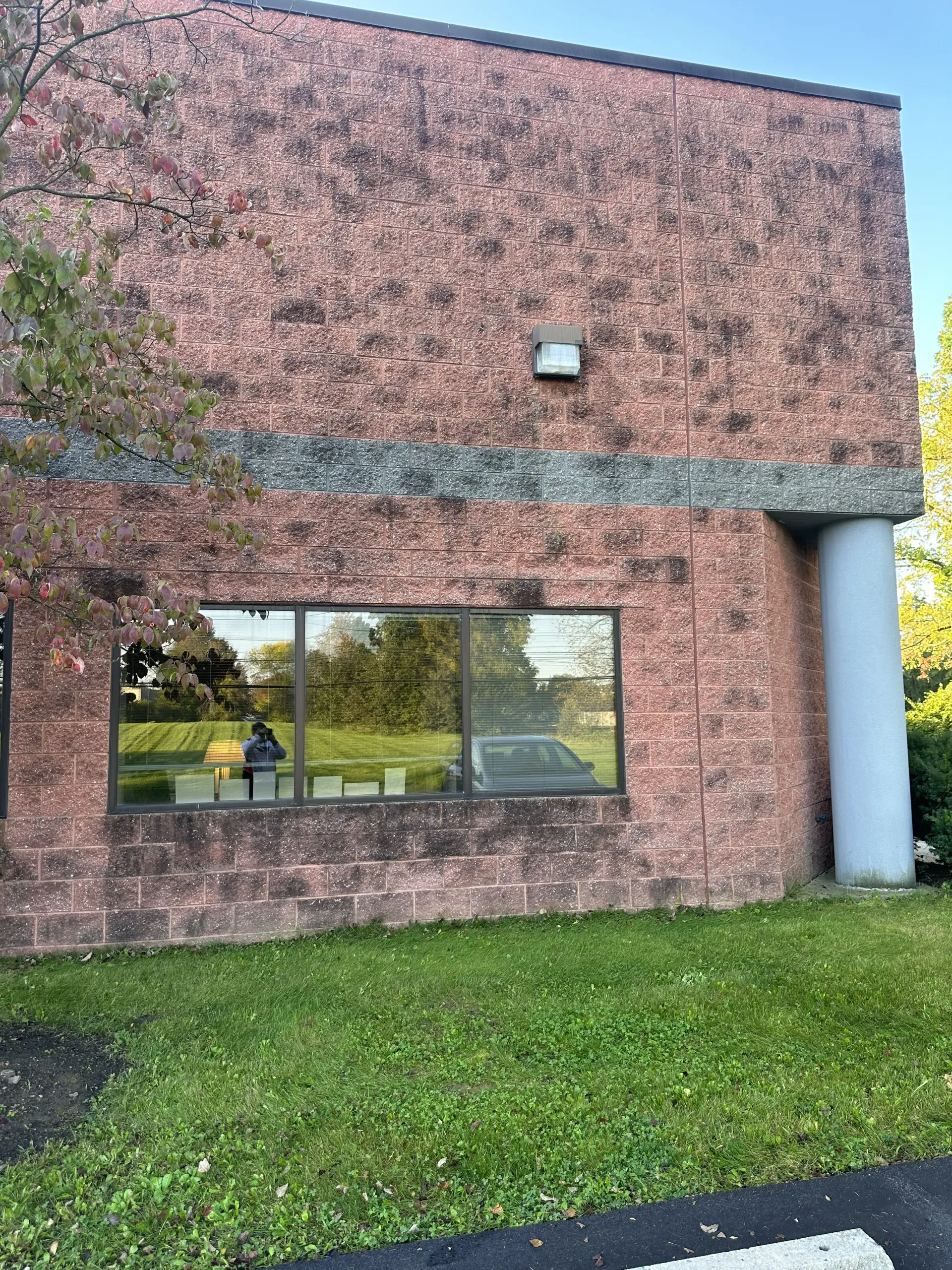 Brick building facade with large window, grassy foreground, and a white column on the right.