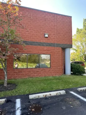 Red brick building exterior with a long window, lawn, and parking spaces in front