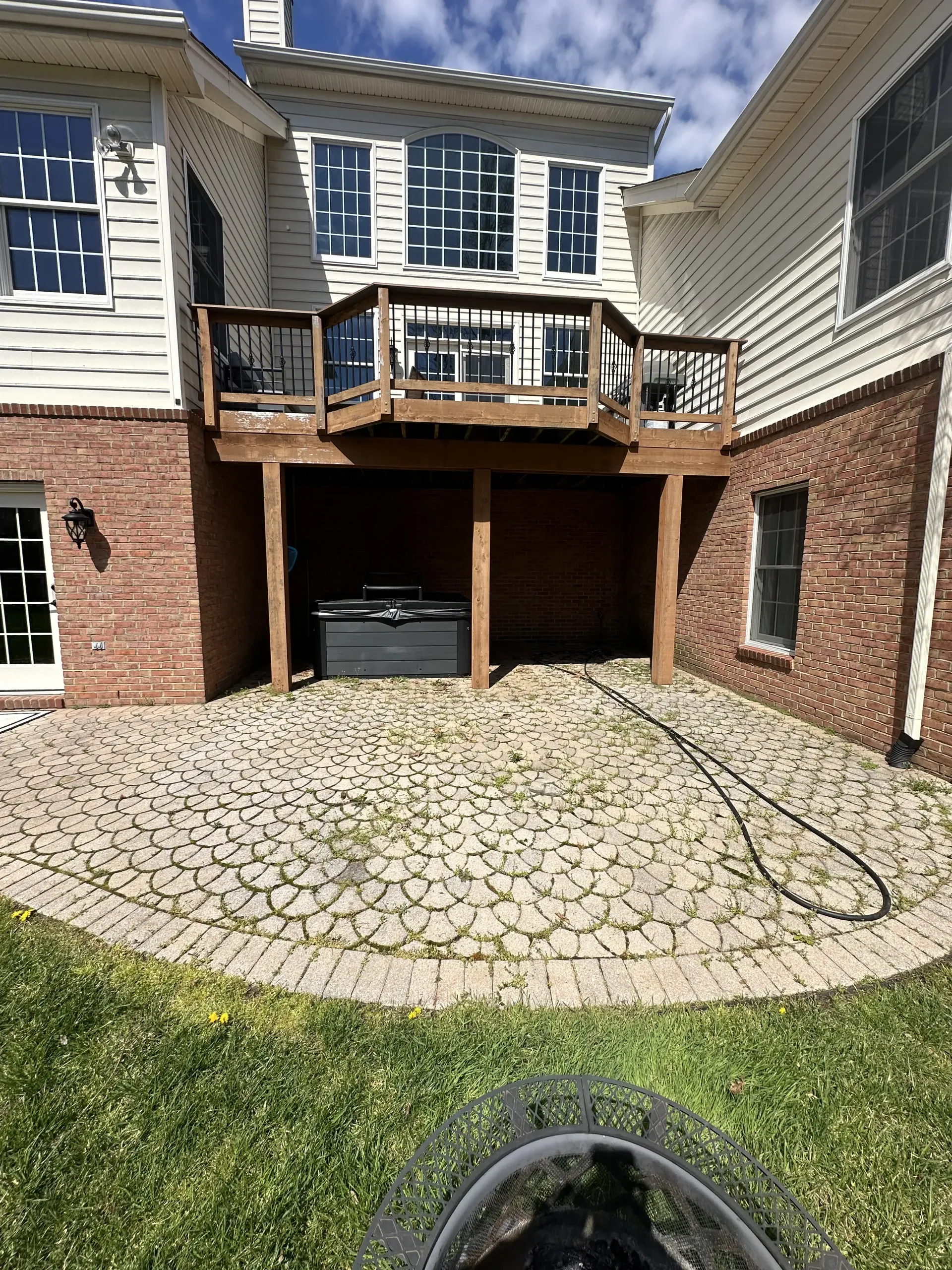 Back patio with brick archway, upper wooden deck, and cobblestone driveway beside a house