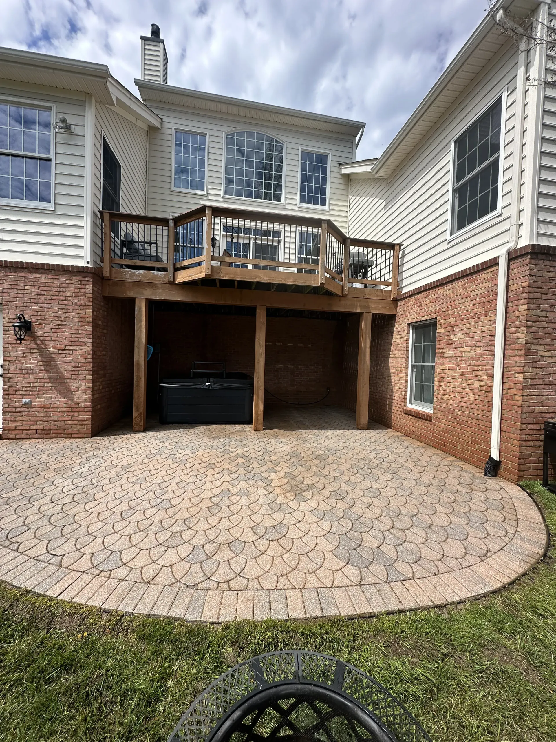 Brick-paved backyard courtyard with a covered carport and wooden deck between two beige townhomes.