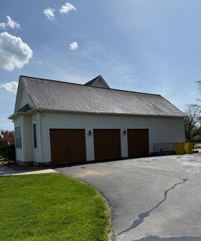Damaged white garage with brown doors and a collapsed roof beside a curved driveway under a blue sky
