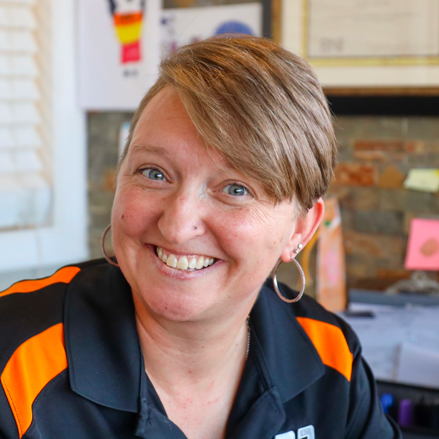 A woman wearing a black and orange shirt and hoop earrings is smiling.