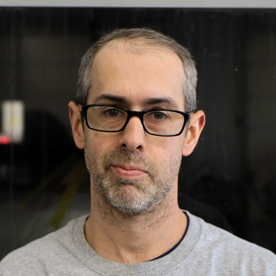 A man with glasses and a beard is wearing a grey shirt.