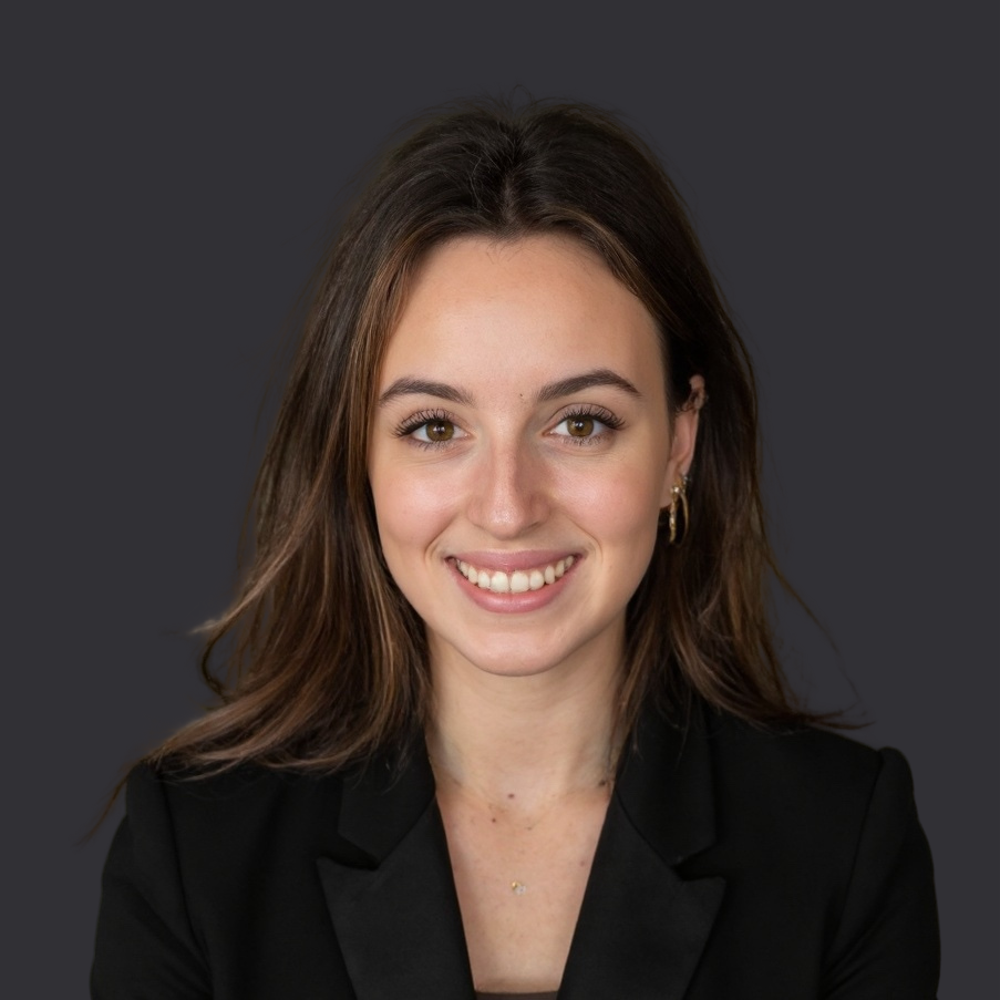 Woman in black blazer smiling at the camera against a gray background.