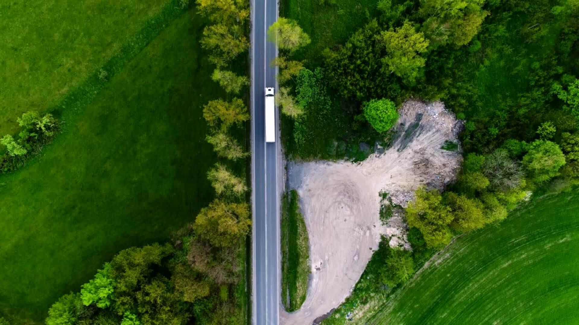 Vue aérienne d'un semi-remorque blanc circulant sur une route traversant un champ vert.