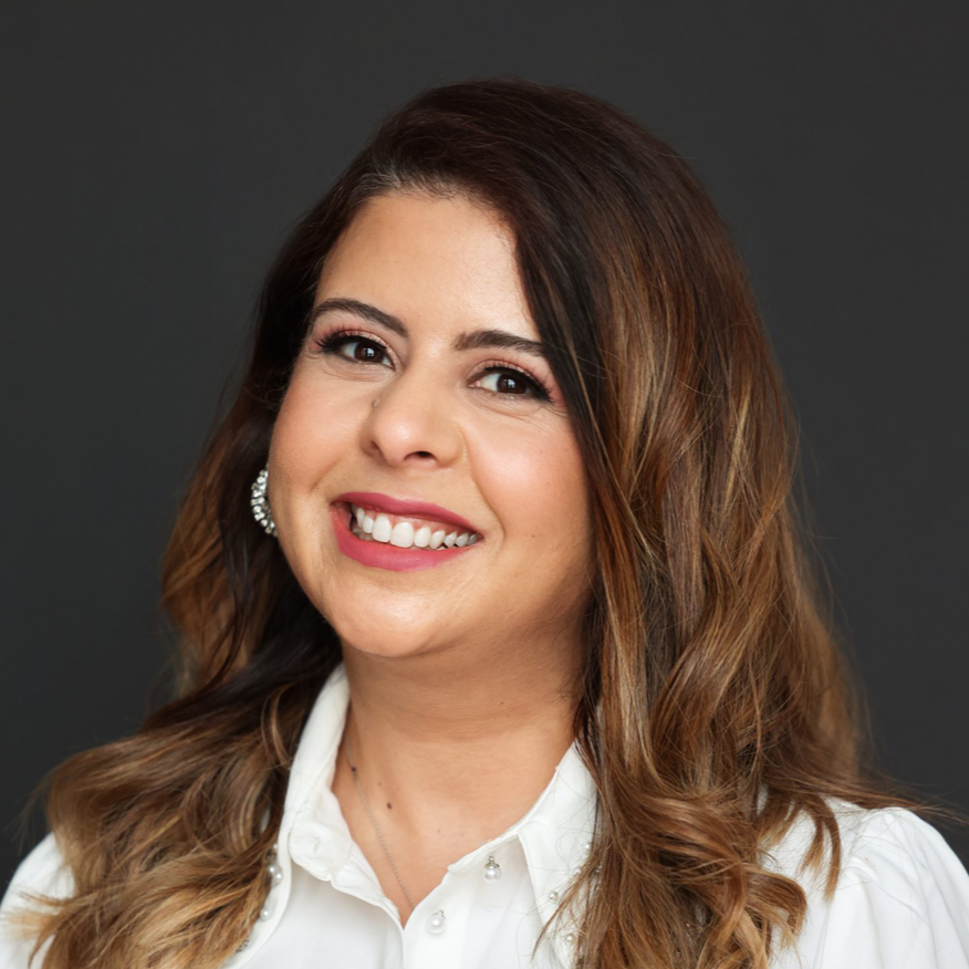 Woman with brown hair smiles, wearing white shirt, against a dark grey background.