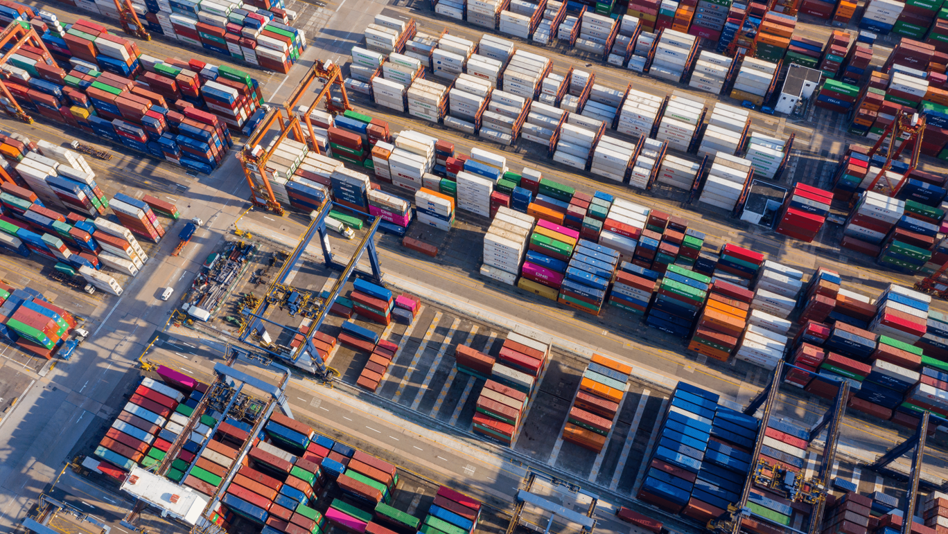 Vue aérienne d'un port de commerce animé avec des rangées de conteneurs de marchandises colorés.