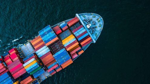 Aerial view of a cargo ship loaded with colorful shipping containers sailing on dark blue water.