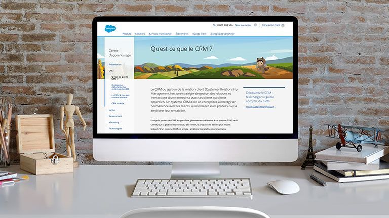 Ordinateur de bureau affichant une page web Salesforce intitulée « Qu'est-ce que le CRM ? » sur fond de mur de briques.