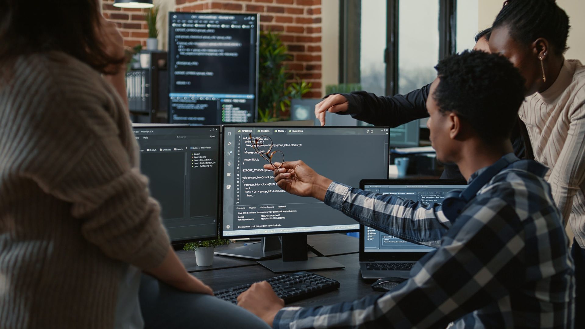 Colleagues collaborating around computer monitors in an office, pointing at code on a screen