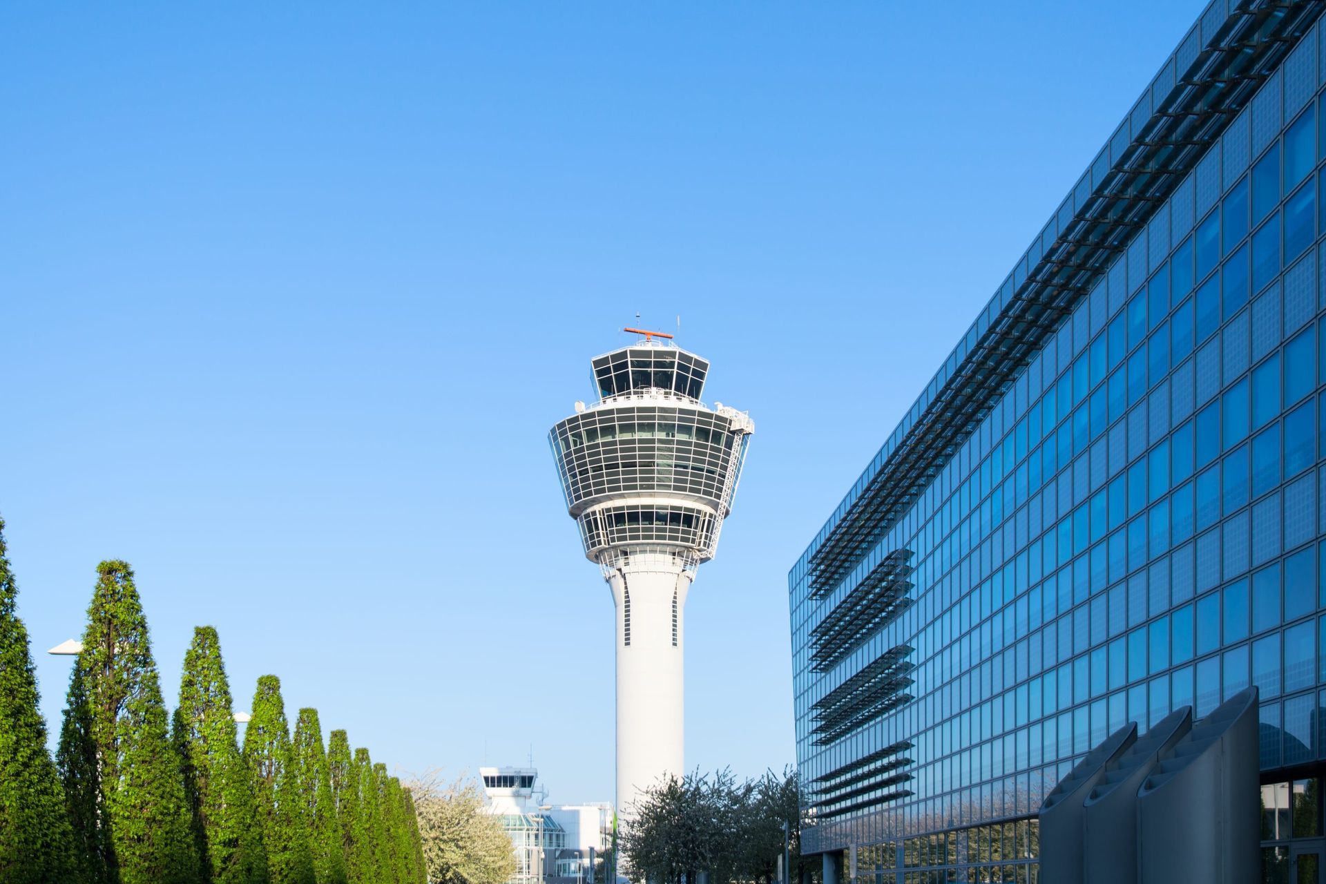 Tour de contrôle de l'aéroport et bâtiment moderne en verre se détachant sur un ciel bleu azur.