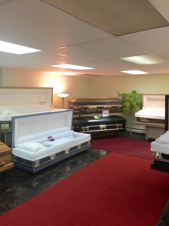 Funeral showroom with open casket displays on red carpet and beige walls