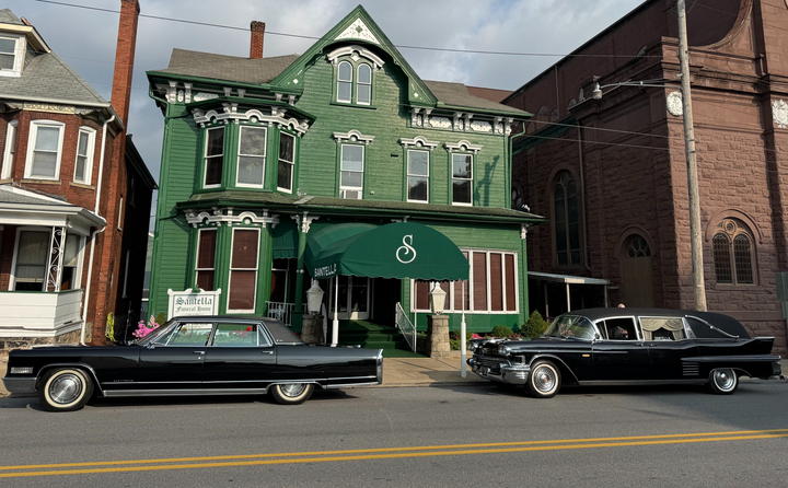 Green Victorian-style storefront with white trim and a teal awning on a city street