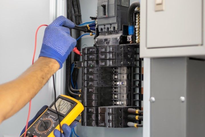 Technician testing an electrical breaker panel with a multimeter and gloved hand