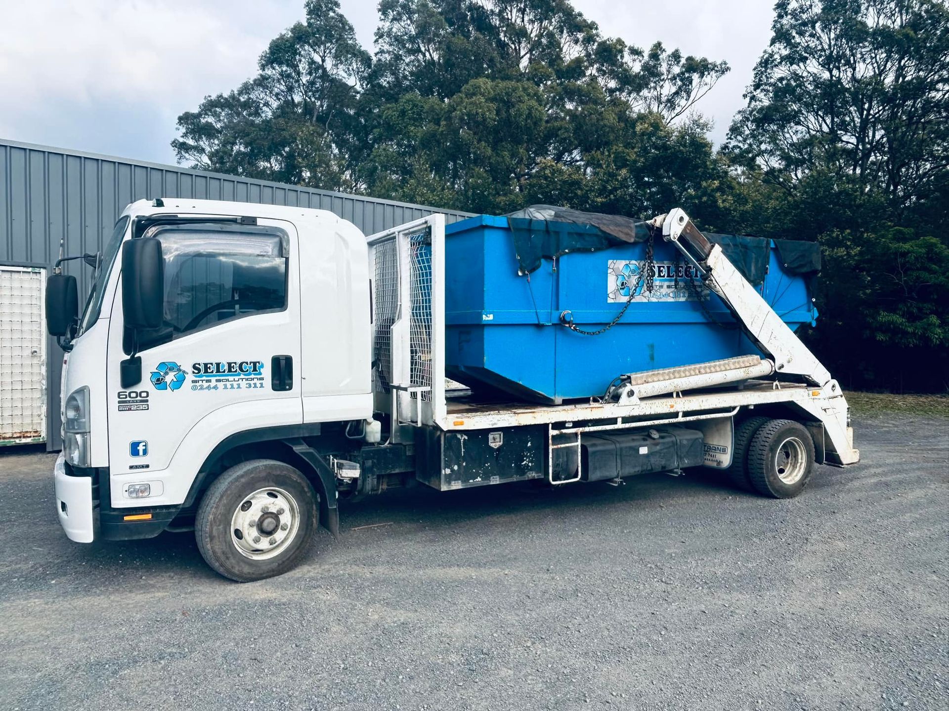 White truck with a blue dumpster loaded on its flatbed, parked on gravel. — Select Site Solutions in Ulladulla, NSW