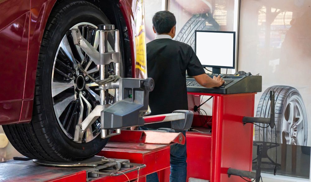 Mechanic using wheel balancer on a car tire in an auto shop, with computer monitor and red equipment
