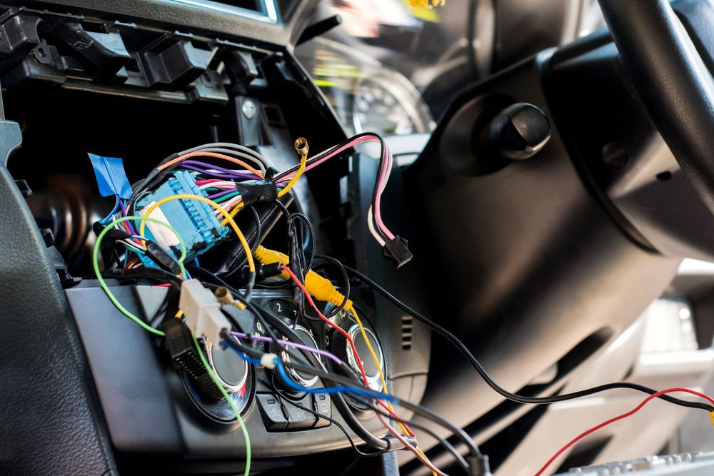 Tangled multicolored wires inside a car dashboard, exposing the steering column and interior panels