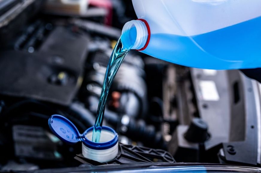 Blue coolant pouring into a car engine reservoir with the hood open