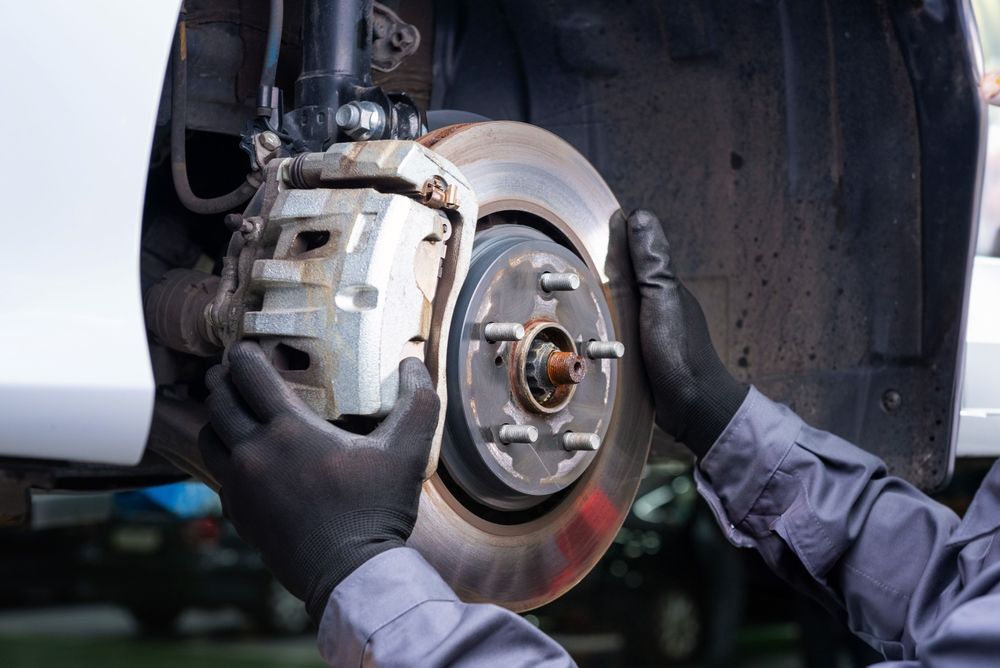 Mechanic replacing a car brake rotor and caliper with gloved hands in a garage