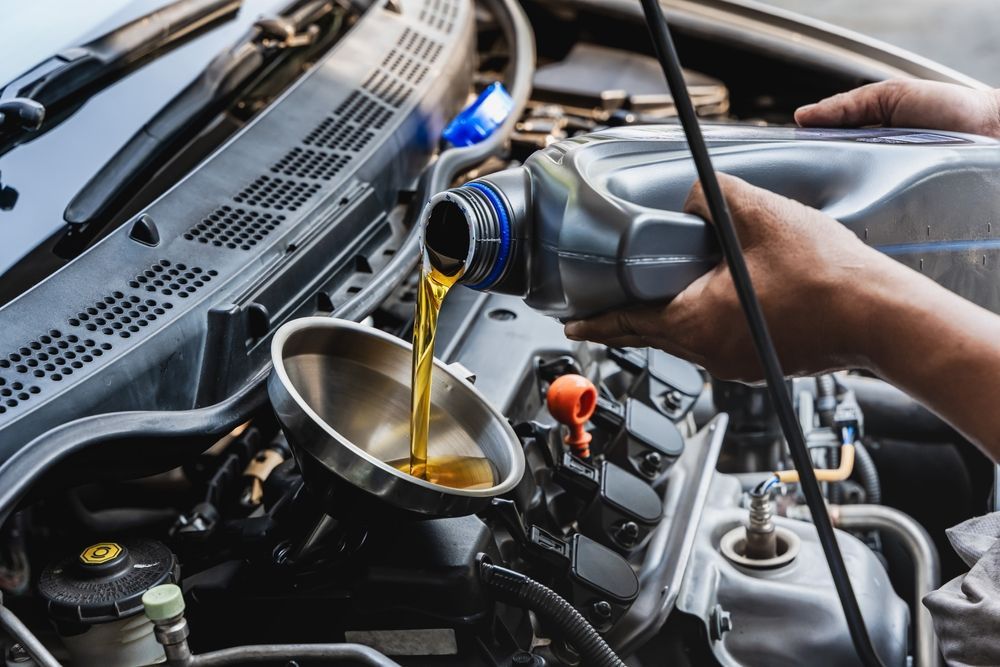 Oil being poured into a car engine through a funnel in the open engine bay.