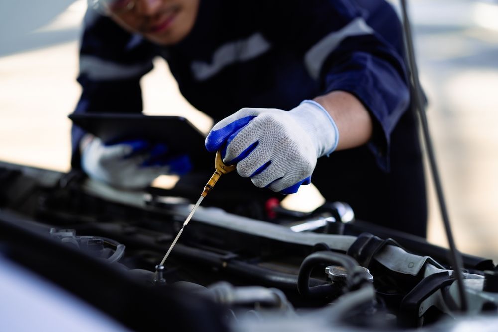 Mechanic using a dipstick to check engine oil under an open car hood
