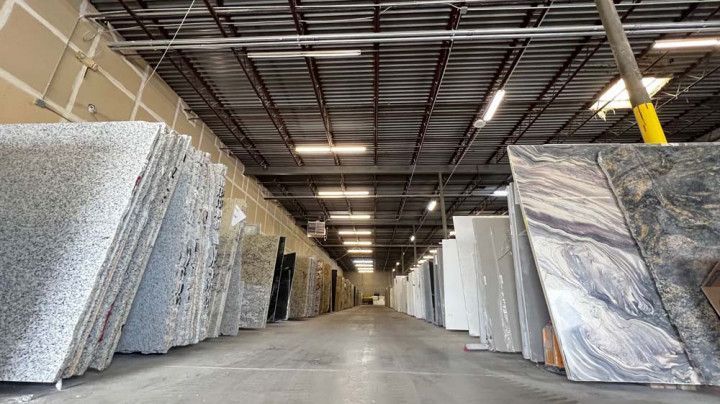 Warehouse interior with granite slabs. Gray and white slabs line the walls, bright ceiling lights.