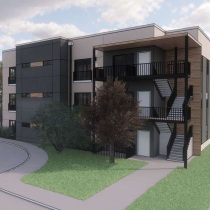 Modern multi-story apartment building with exterior stairwells, landscaping, and driveway.