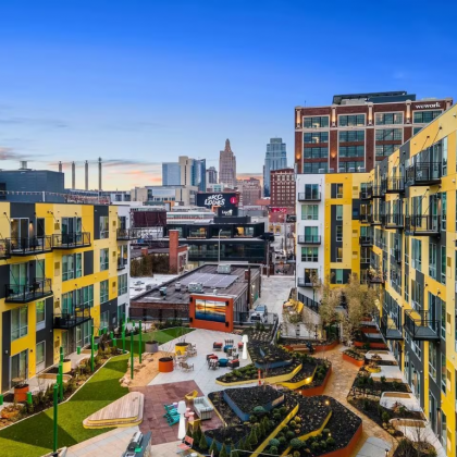 View of a courtyard with yellow and black apartment buildings, with a city skyline in the background.