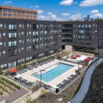 Apartment complex with a pool, lounge chairs, and red furniture on a sunny day.