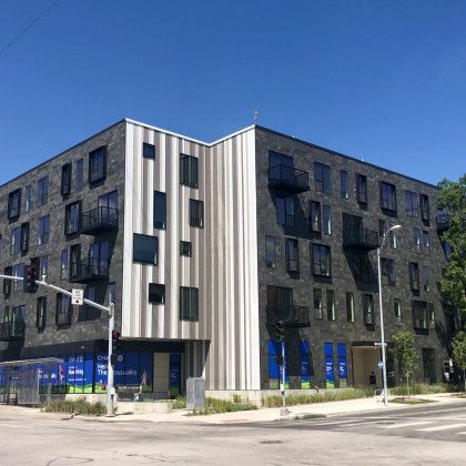 Modern black brick building with white metal paneling on the corner under a blue sky.
