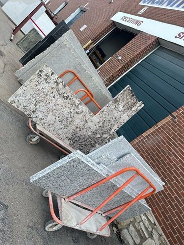 Two hand trucks stacked with granite slabs outside a brick building.
