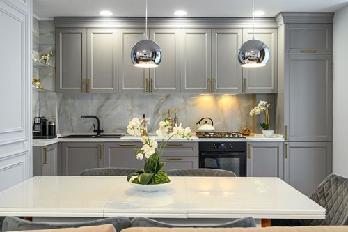 Gray kitchen with white marble backsplash, gold hardware, and two chrome pendant lights.