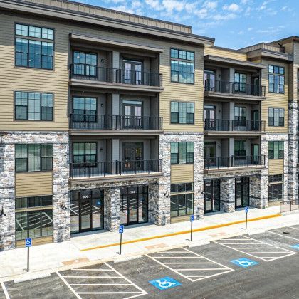 Multi-story apartment building with stone and tan siding, balconies, and accessible parking spaces.