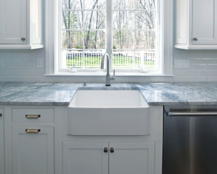 White kitchen with farmhouse sink, window, stainless steel dishwasher, and blue countertops.
