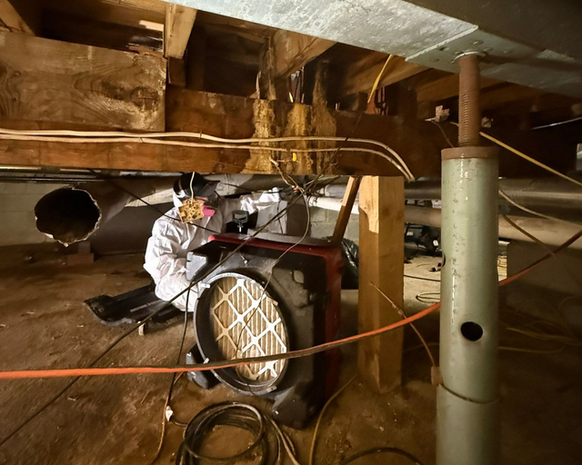 K.O.S. Restoration technician in PPE running a HEPA air scrubber during mold remediation in a Suffolk County crawlspace