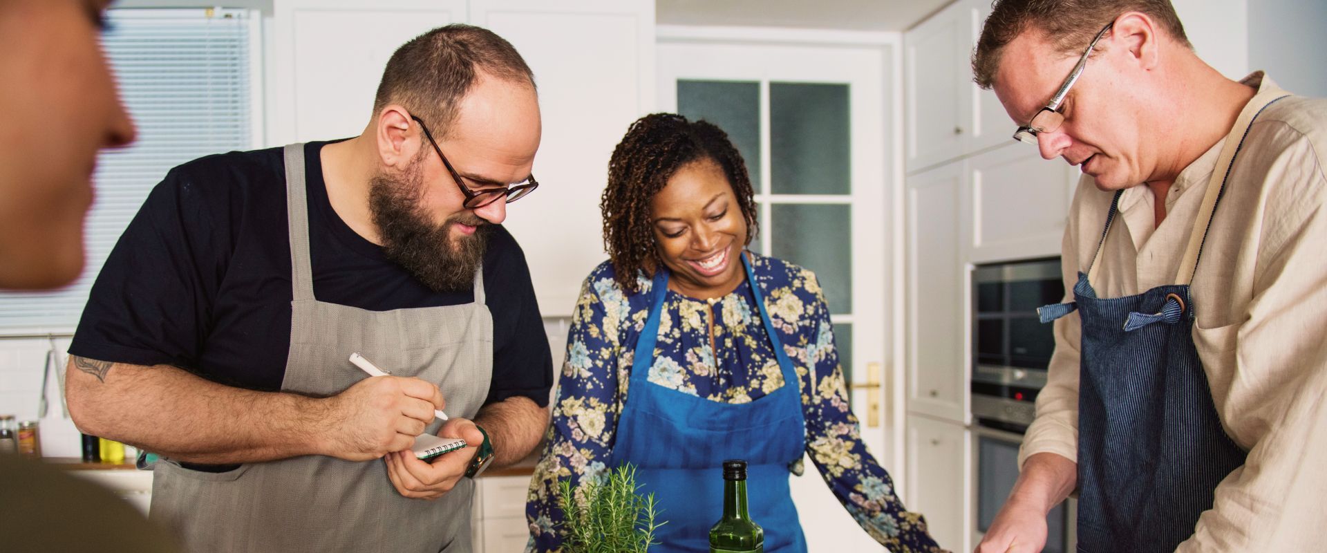 Three people gather around a kitchen counter, smiling and preparing food together.