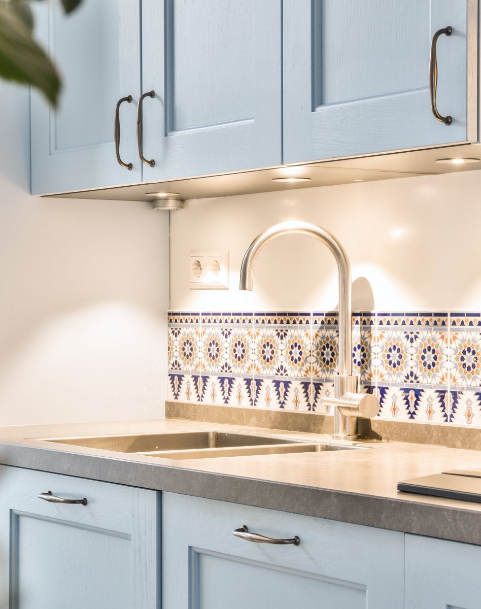 Light blue kitchen cabinets, stainless faucet, and patterned tile backsplash over a sink.