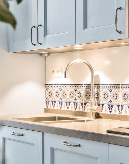 Light blue kitchen cabinets, stainless faucet, and patterned tile backsplash over a sink.
