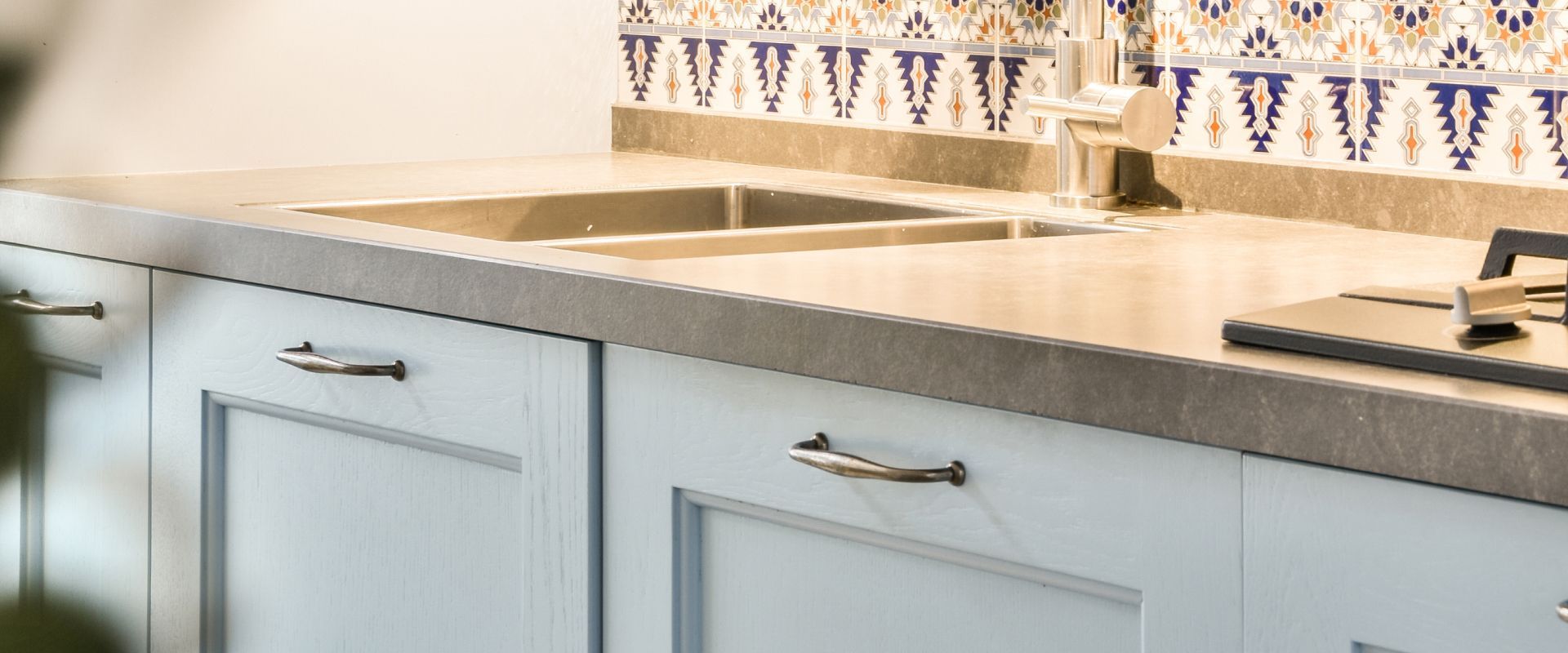 Light gray kitchen cabinets with a countertop and sink under tiled backsplash
