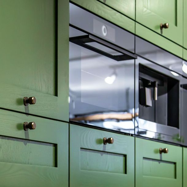 Green kitchen cabinets with a stainless steel built-in oven and microwave behind reflective glass doors