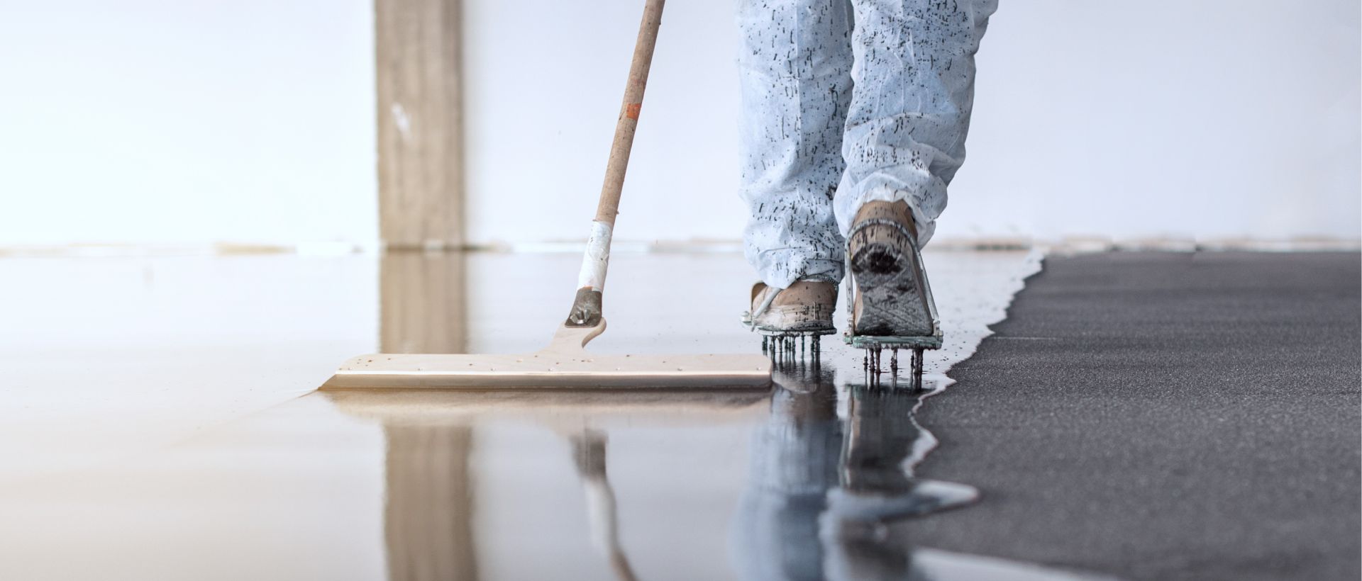 Person applying gray floor coating with a roller, reflecting on the glossy wet surface