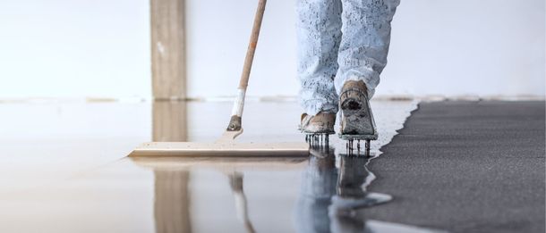 Person applying gray floor coating with a roller, reflecting on the glossy wet surface