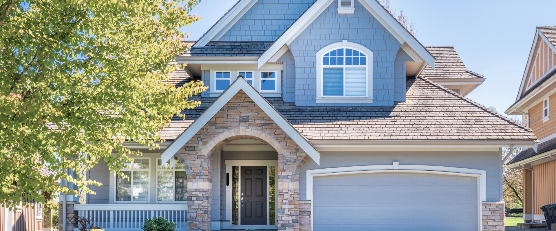 Blue suburban house with stone trim, garage, and front porch under bright daylight