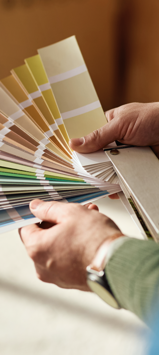 Hands flipping through a fan of paint color swatches in a store
