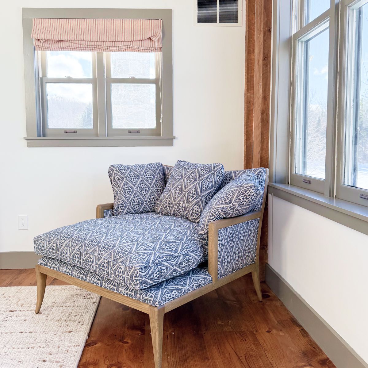 Blue patterned chaise lounge by bright windows in a sunlit room with wood floors.